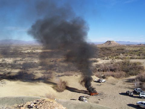 1981 Ford F-150 - A vehicle is engulfed in flames and smoke in a desert environment with other vehicles present.