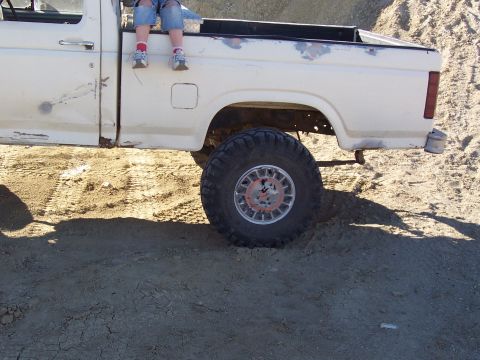 1981 Ford F-150 - A child sits on the edge of a white pickup truck bed, with large off-road tires visible.
