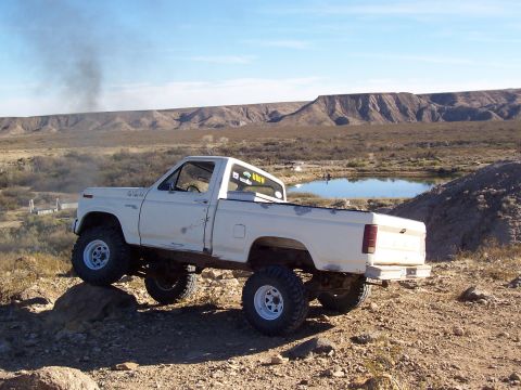 1981 Ford F-150 - A white pickup truck navigates a rocky, off-road landscape with a pond in the background.