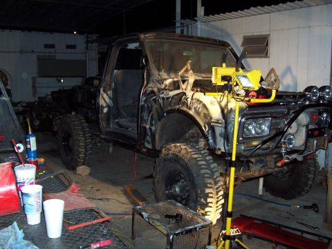 1981 Ford F-150 - A heavily modified pickup truck sits in a workshop, surrounded by tools and supplies, suggesting ongoing customization or repair work.