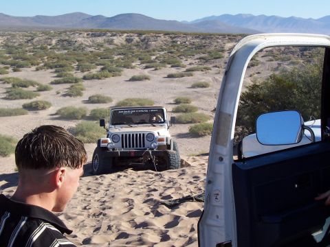 1981 Ford F-150 - A white Jeep Wrangler navigates sandy terrain, with a tow strap attached to its front bumper.