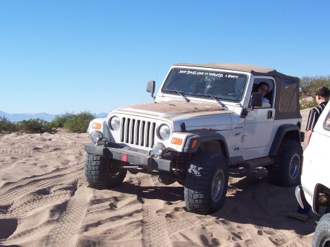 1981 Ford F-150 - A white Jeep Wrangler navigates sandy terrain under a clear blue sky.