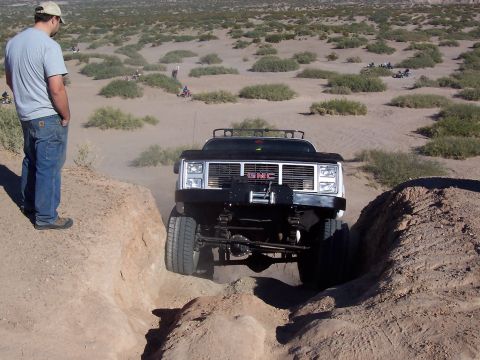 1981 Ford F-150 - Off-road GMC pickup truck navigating a challenging dirt path with a person observing.