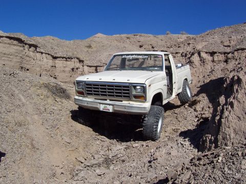 1981 Ford F-150 - White Ford pickup truck navigates a steep, rocky incline under a clear blue sky.
