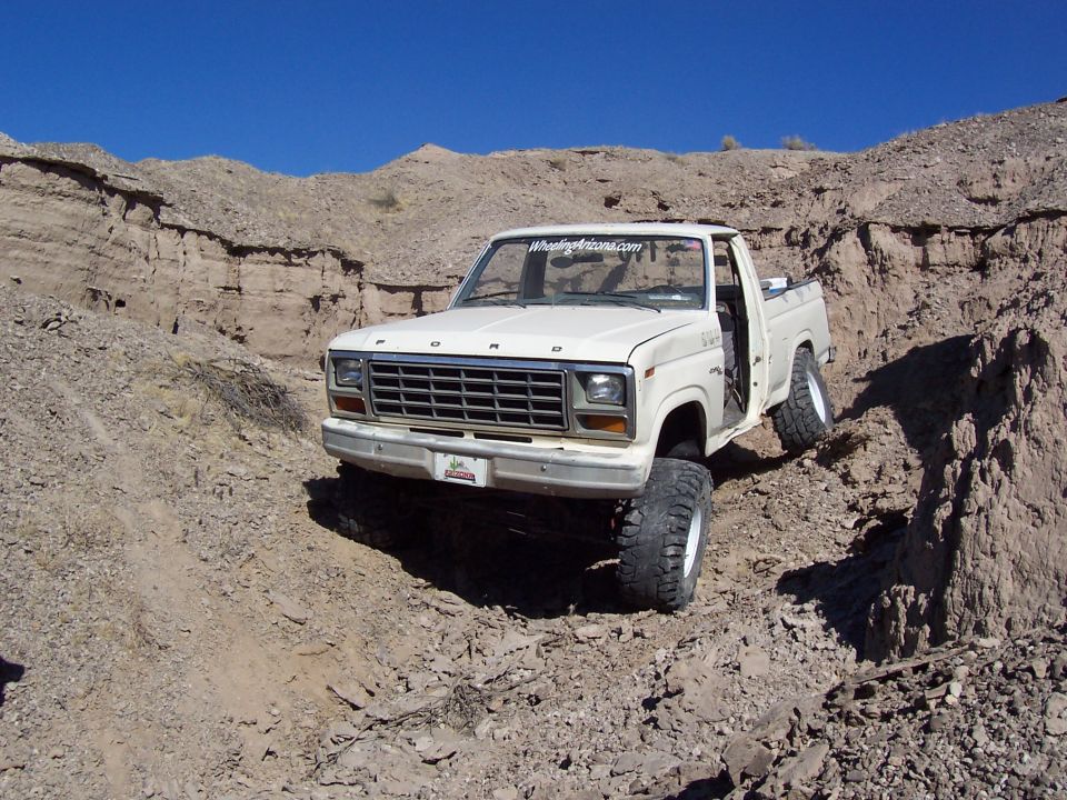 White Ford pickup truck with large tires on a dirt hill
