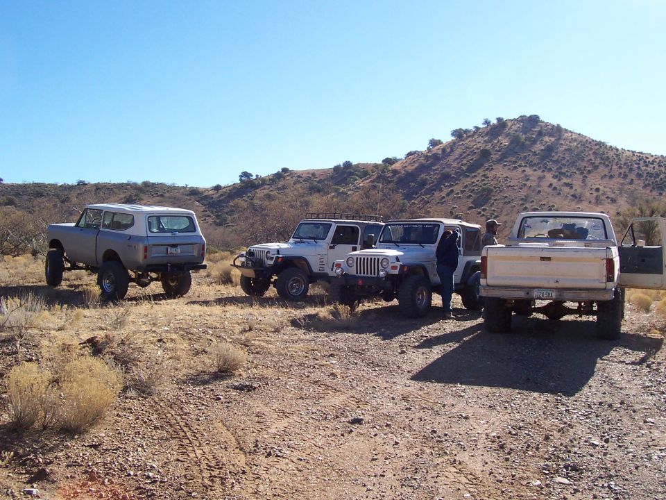 Lifted white Scout, two Jeep Wranglers and a doorless Ford pickup staged on a desert trail