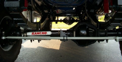 Undercarriage view of a truck's front axle and suspension with a Rancho steering stabilizer