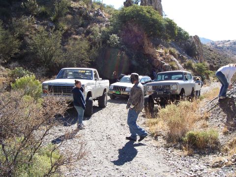 1981 Ford F-150 - A group of people and several off-road vehicles are gathered on a dusty trail in a rocky, arid landscape.