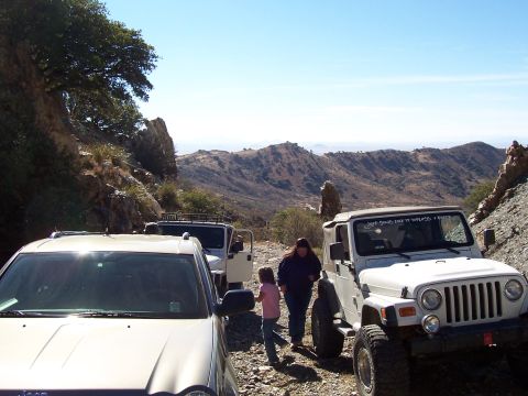 1981 Ford F-150 - Several SUVs are stopped on a mountain road, with people interacting near the vehicles.