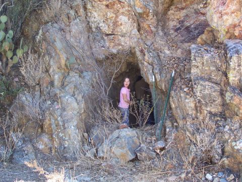 1981 Ford F-150 - A young girl stands at the mouth of a rocky cave, surrounded by desert vegetation.