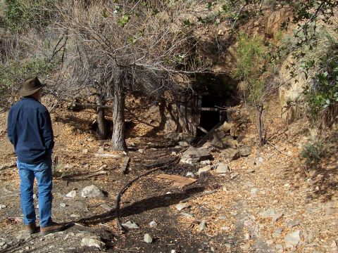 1981 Ford F-150 - A person observes the entrance to an old mine, surrounded by dry brush and rocky terrain.