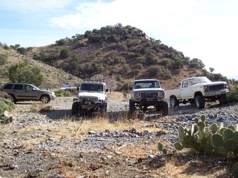 1981 Ford F-150 - A white pickup truck is parked on a rocky incline alongside other off-road vehicles.