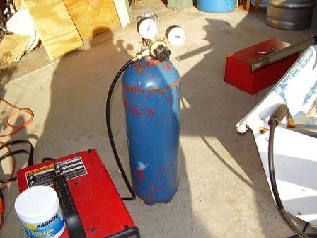 2004 Aston Martin Virage - A blue gas cylinder and red welding machine are set up on a concrete surface next to a white boat hull section.