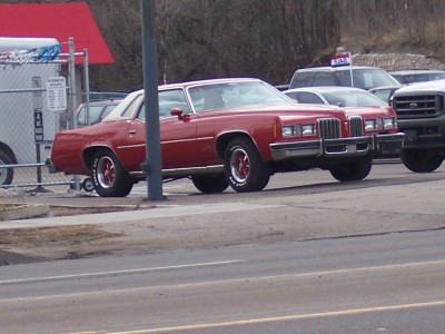 1972 Ford Ranchero - A red sedan with a white vinyl roof is parked next to other vehicles on a lot.
