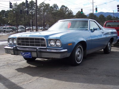 1972 Ford Ranchero - A blue 1972 Ford Ranchero is seen from a three-quarter front angle, with a red truck partially visible behind it.