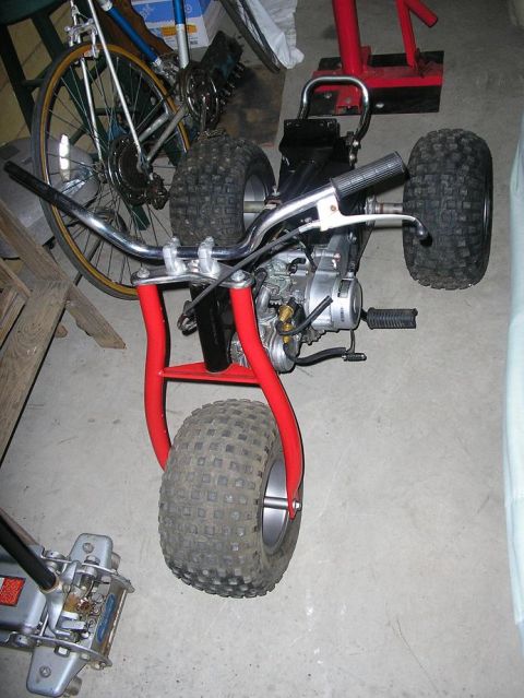 1900 Honda Big Red - A red three-wheeler ATV with knobby tires and chrome handlebars is parked indoors.