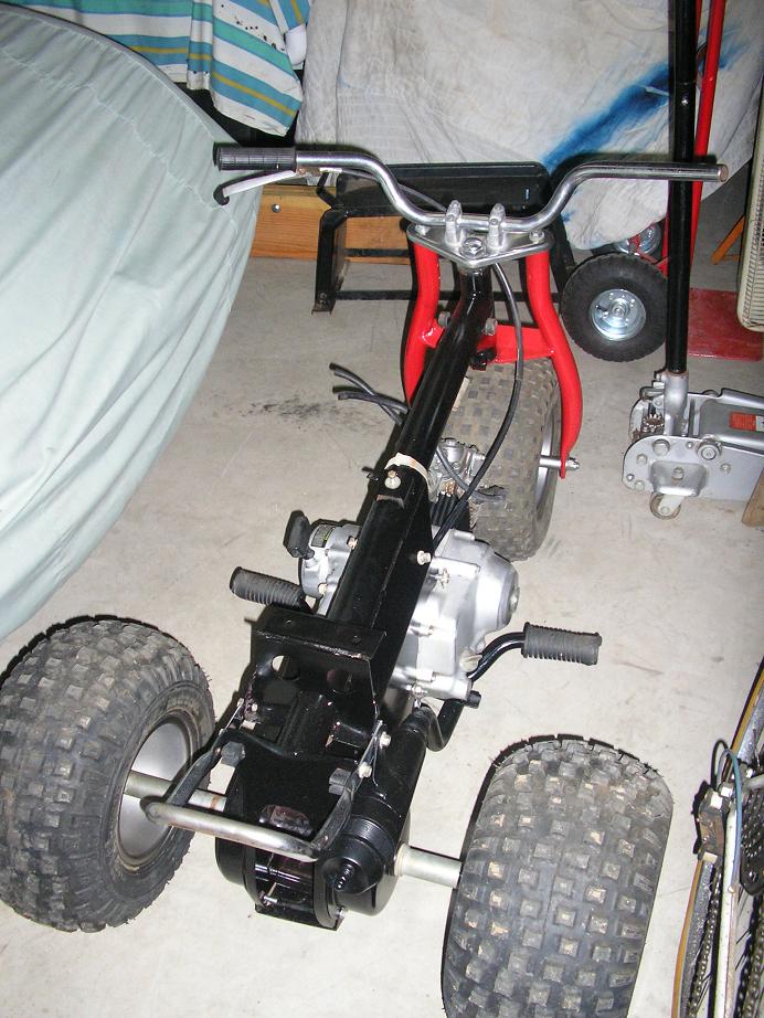 Three-wheeled ATV with black frame and red front forks, knobby tires, and handlebars