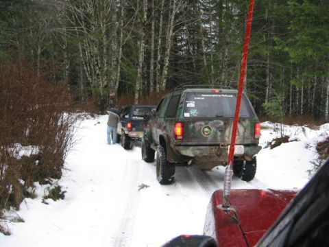 1991 Ford Explorer - A line of SUVs, including a camouflaged 1991 Ford Explorer, navigate a snowy trail in a forest.