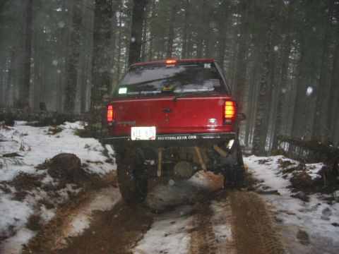 1991 Ford Explorer - A red SUV navigates a muddy and snowy path through a dense forest.
