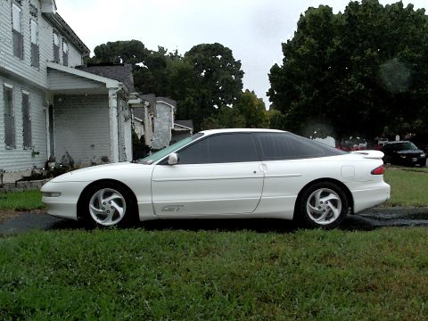 1996 Ford Probe - A white 1996 Ford Probe GT is parked on the grass next to a weathered house, with a dark SUV visible in the distance.