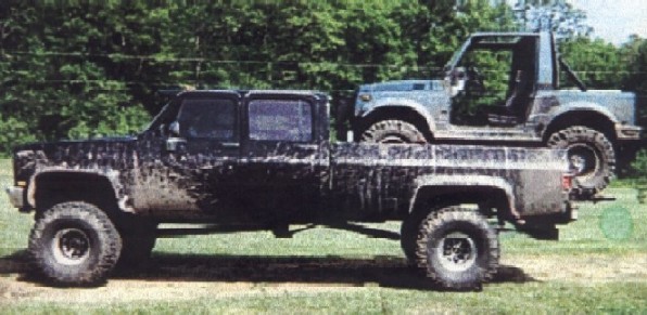 Side view of a muddy black pickup truck carrying a small SUV in its bed