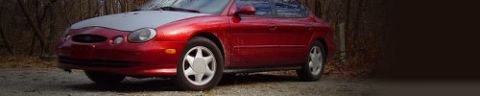 1997 Ford Taurus - Red 1997 Ford Taurus sedan with a silver hood is parked on a gravel surface.