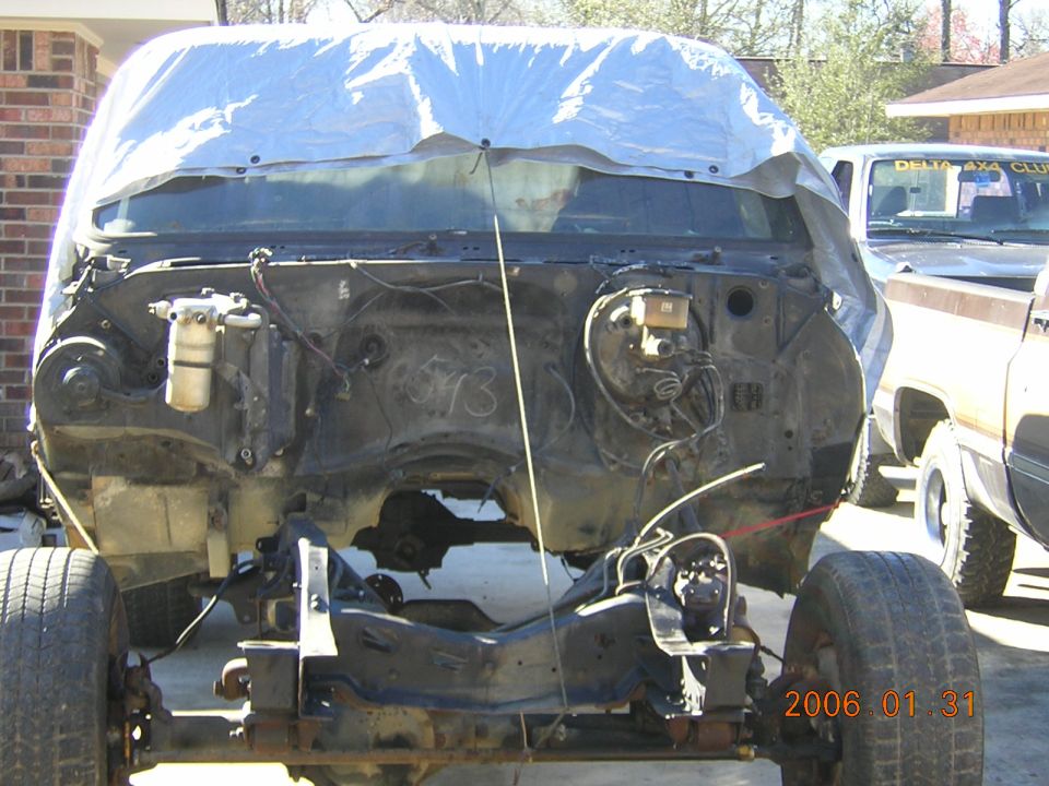 1986 Chevrolet Blazer chassis with engine bay exposed, tarp over windshield. Another truck is parked to the right