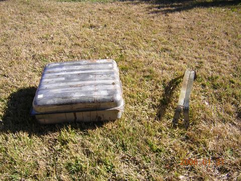 1986 Chevrolet Blazer - A metal fuel tank and two brackets sit on dry grass under a sunny sky.
