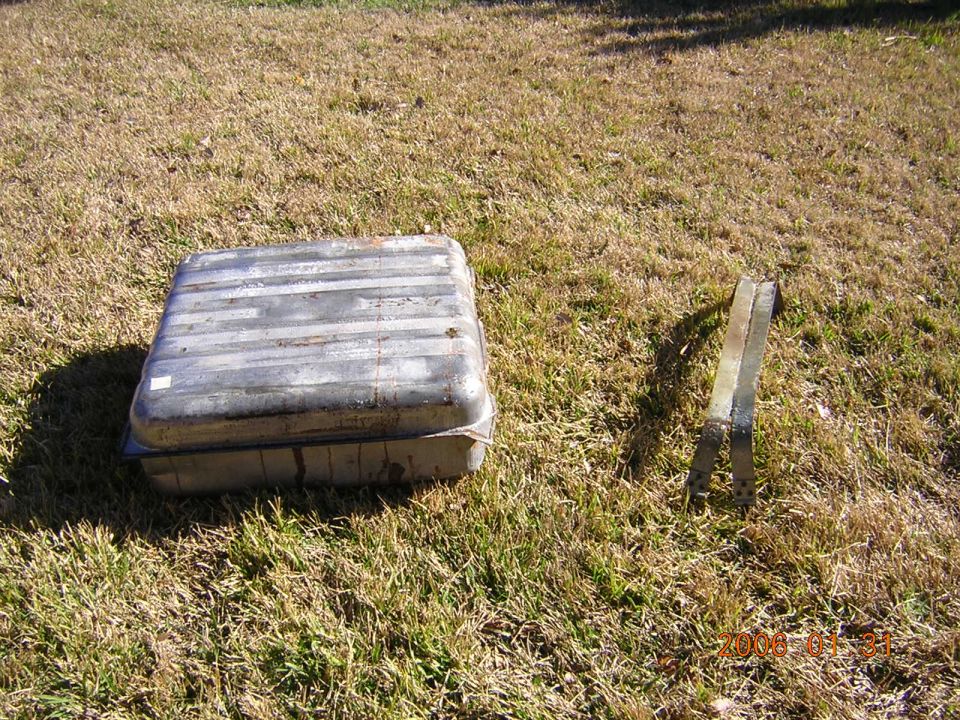 Metal fuel tank with horizontal bands, next to two metal brackets on dry grass