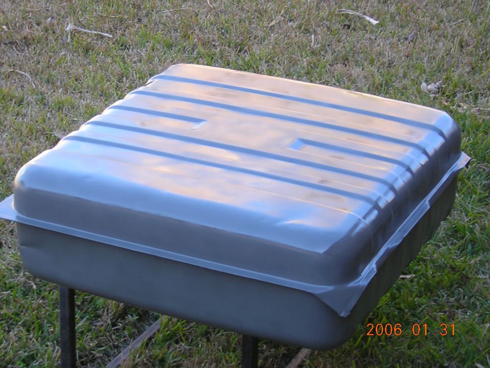 Gray metal fuel tank with horizontal ridges, resting on metal legs outdoors