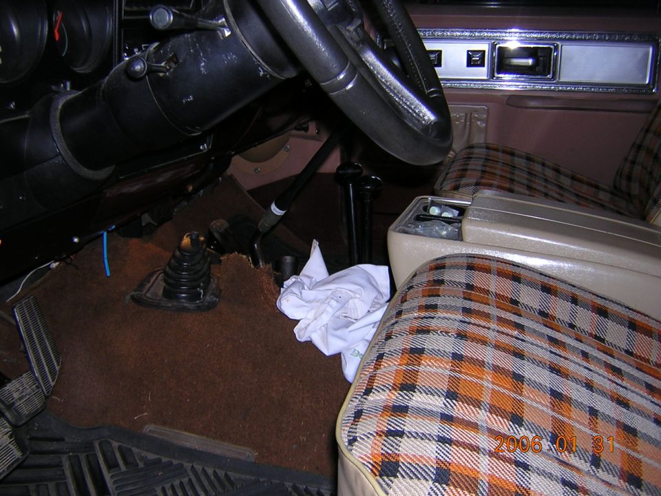 Interior shot of a vehicle with plaid seats, a steering wheel, and a gear shift. There's a white cloth on the floor