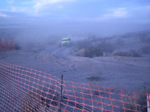 Green off-road buggy on a dusty desert trail behind orange fencing in hazy light