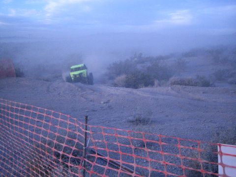 Green off-road buggy turning on dusty desert course behind orange fence at dusk