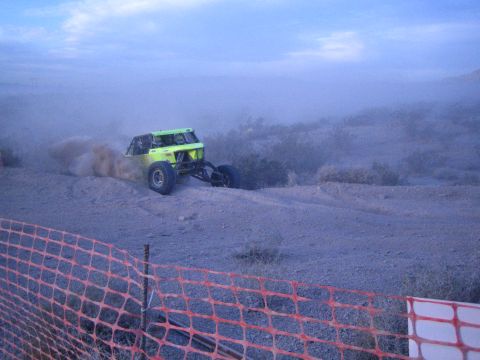 Green off-road buggy sliding sideways throwing dust behind orange fence in desert