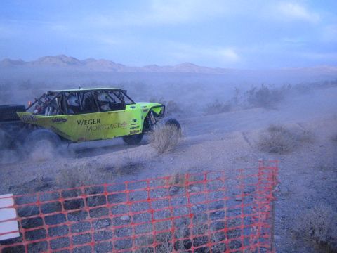 Green Weger Mortgage off-road buggy raising dust on desert course past orange fence