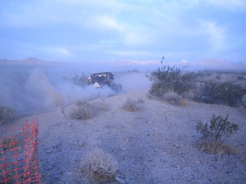 Off-road vehicle with headlights on a dusty desert trail at dusk