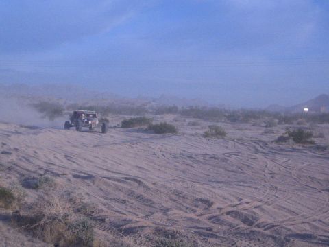 Red open-wheel off-road buggy on sandy desert flat with mountains behind