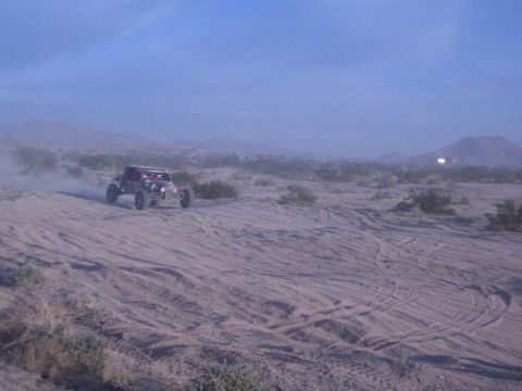 Red off-road buggy raising dust on sandy desert course with hills behind