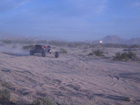 Red off-road buggy on tire-marked sandy desert with distant mountains