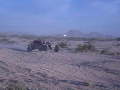 Open-wheel off-road buggy turning on sandy desert flat with mountains behind