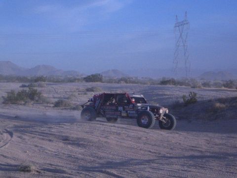 Off-road race buggy under power line tower on dusty desert course