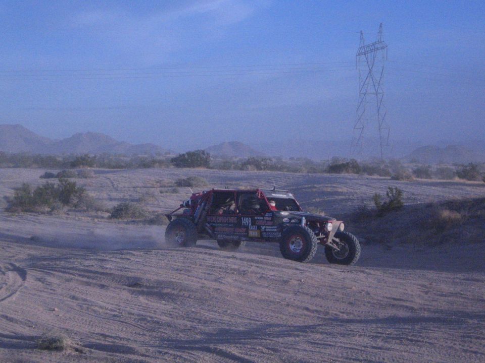 Off-road race buggy under power line tower on dusty desert course