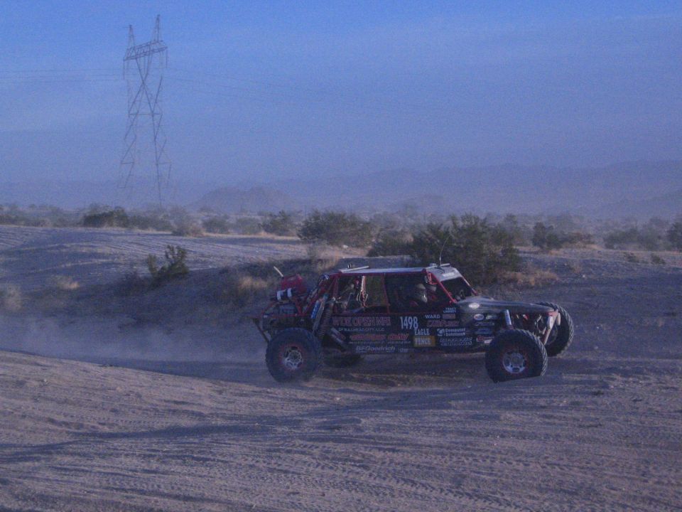 Off-road race buggy number 1498 on dusty desert track with power tower behind