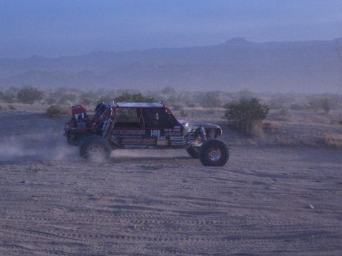 Off-road race buggy number 1498 throwing dust on desert flat at dusk