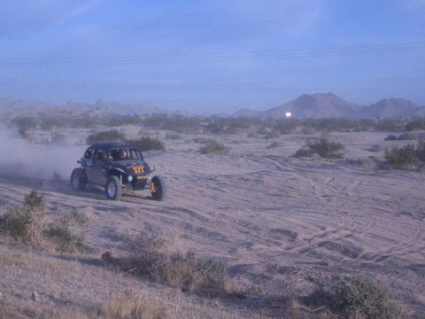Off-road buggy number 517 raising dust on sandy desert course at dusk