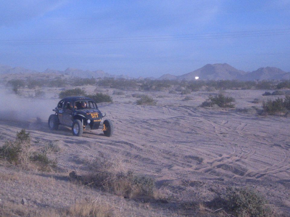 Off-road buggy number 517 raising dust on sandy desert course at dusk