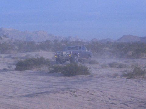 Off-road truck with headlights on in hazy dusty desert at dusk