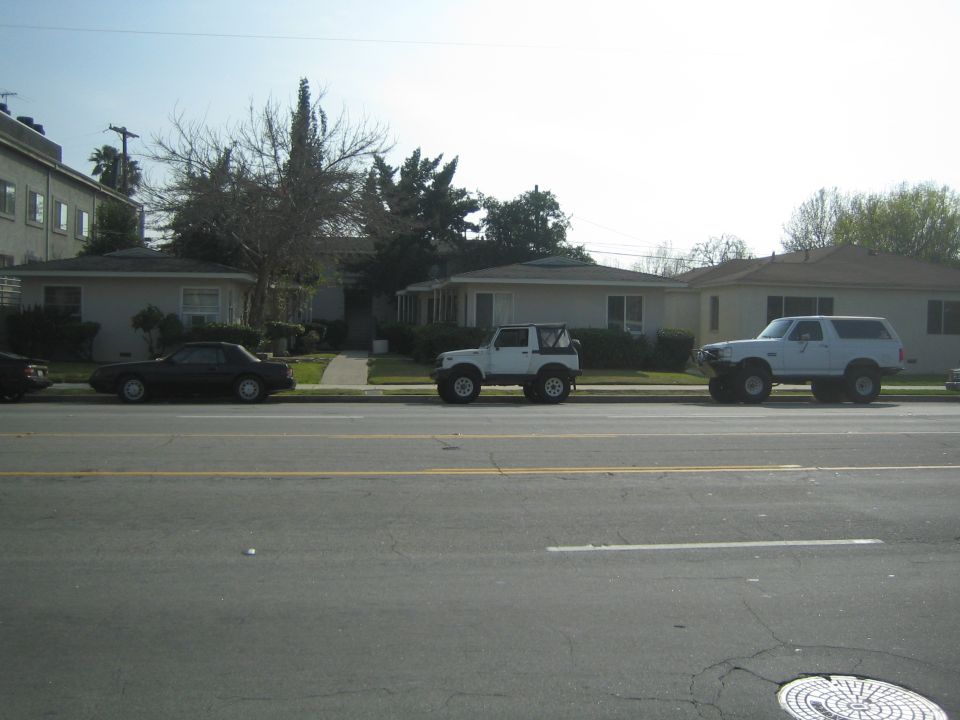White Suzuki Samurai with lifted suspension and off-road tires parked on a residential street