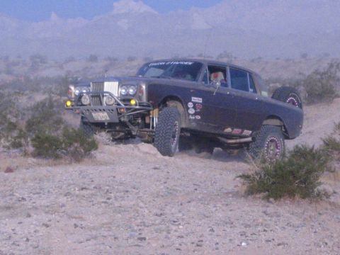 Dark off-road racing sedan with tube front bumper and tall tires climbing desert terrain