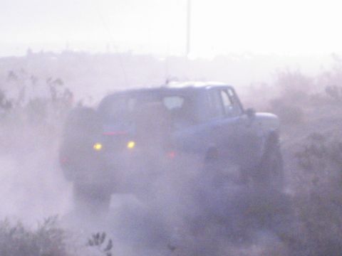 Off-road car emerging from thick dust cloud with two yellow lights lit in desert